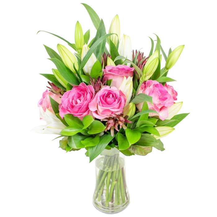 A lush, composed bouquet of deep pink roses and white lilies rests in a simple, clear glass vase, captured on a bright white background that isolates every delicate nuance of colour and texture. The composition is led by several large, fully-bloomed roses whose velvety petals reveal a spectrum from intense fuchsia to pale blush; each bloom has a layered, tactile quality that suggests a soft, familiar fragrance. Interlaced among these are elegant lily buds-many still tightly closed, a few beginning to open-their long, tapered forms and subtle green tips hinting at the trumpet-shaped blooms to come and a refined, powdery perfume. The flowers are cradled by abundant greenery: broad, glossy leaves give structure and shine while finer, lighter sprigs weave through to add movement and air. Small, darker reddish-brown filler elements are thoughtfully placed to introduce contrast and depth, preventing the palette from feeling overly light. The vase is transparent with a gently tapered base and holds clear water, through which the clean-cut stems are plainly visible, reinforcing the workmanlike care of the arrangement. The overall silhouette is full and rounded, deliberately balanced to read beautifully from every angle-ideal as a centrepiece on a dining table in a Golders Green home or as a heartfelt gift delivered to a flat near the tube station or a family gathering at the nearby synagogue. The feeling conveyed is one of celebration and sincere attention: a bouquet that looks as if it was assembled with quiet expertise, inviting touch, scent and lingering appreciation.