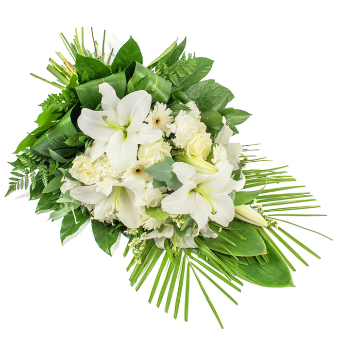 An elegant, elongated funeral spray in pristine white and layered greens is photographed against a clean white background, allowing every detail of the floristry to stand out as if resting in soft chapel light. The design flows from a generous cluster of blooms at the upper left, tapering gracefully down to a narrower point at the lower right, creating a gentle diagonal that suggests a final, peaceful journey. At the centre, several majestic white lilies open into broad trumpets, their petals smooth and gently reflexed, while a few tightly held buds rise above, promising a slow, dignified unfolding. Surrounding these focal flowers are creamy roses in various stages of bloom, from compact buds to more open rosettes, accompanied by white carnations whose frilled petals lend a cloud-like softness, and daisy-shaped white gerberas with discreet yellow or darker centres. Tiny stems of white filler flowers tuck into the gaps, giving the arrangement a light, airy texture without disturbing its formal structure. A rich underlay of greenery shapes the spray: wide, glossy dark green leaves frame the flowers and anchor them visually, while delicate fern fronds and muted blue-green eucalyptus leaves contribute contrast in both texture and tone. Near the top, long slender leaves are folded and bundled into neat vertical lines, adding a sense of crafted precision. From the lower right corner, a fan of slender palm fronds extends outward, echoing the curve of a feather and emphasising the spray's contemporary, one-sided profile. The effect is a calm, dignified tribute, ideal as a sympathy arrangement for a funeral service in Golders Green, whether placed beside the coffin or on a stand in a quiet room of reflection.