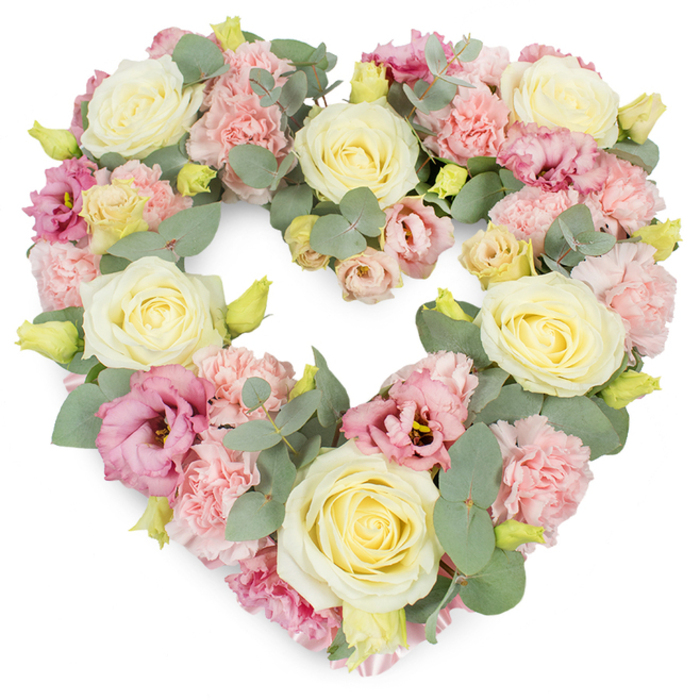 This image shows a luxurious heart-shaped funeral wreath, carefully constructed so that the flowers form a seamless, continuous heart against a clean white background. The design is dominated by several large, fully open roses in tones of cream, ivory, and pale buttery yellow, each bloom packed with velvety petals that curl in tight, refined spirals before softly relaxing at the outer edges. Interwoven among these central roses are numerous heads of soft pastel pink carnations, their delicate, frilled petals giving the arrangement a gentle, almost feathery texture. Scattered through the pastel softness are deeper touches of colour from magenta and mauve-pink lisianthus, or eustoma, whose more open, layered blooms and occasional darker centres bring subtle contrast and visual depth. A network of silvery-green eucalyptus foliage runs throughout the heart, the rounded leaves and slender stems creating cool, calming intervals of greenery between the flowers while also tracing the outer edge of the heart shape with grace and clarity. Tiny yellow-green buds are visible at various points, suggesting freshness and the continuation of life even as the wreath speaks of farewell. The arrangement is tightly packed, leaving no gaps, which enhances its sense of completeness and devotion. As a florist used to preparing tributes for services around Golders Green, from nearby synagogues to quiet family gatherings by the crematorium, I see in this design a gentle expression of sympathy and enduring love. The pastel palette and soft textures convey peace, tenderness, and remembrance, making this heart wreath a meaningful choice for funerals, memorials, or anniversaries when families wish to honour someone cherished with understated elegance.