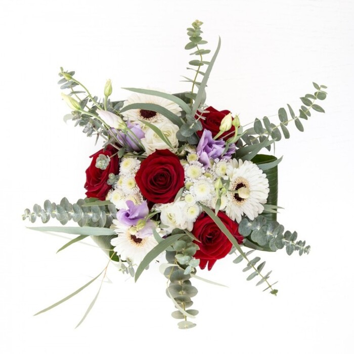 This bouquet, reminiscent of a cherished Golders Green tradition, embodies both poise and presence through its masterful composition. Substantial white gerberas, their bright petals encompassing deep brown centers, provide a foundation of serenity and classic style. Spiraled, velvety red roses rest alongside, their passionate tones conveying affection and heartfelt wishes, perfect for gifting to friends on Finchley Road or welcoming a new neighbor along Golders Green Road. Wispy sprigs of eucalyptus hover overhead, casting subtle shadows and introducing a cool, silvery dimension that invigorates the palette, much like the dappled light filtering through the trees in Childs Hill. Scattered lilac lisianthus add a hint of modernity and intrigue, their soft blossoms and tight buds merging seamlessly into the bouquet and offering a gentle nod to evolving floral design trends. Fluffy white filler flowers contribute a light, airy quality-as if the bouquet itself is filled with laughter and gentle conversation. All these elements are elegantly gathered and anchored by broad, dark green leaves, the arrangement's harmonious finish reflected in the glass vase below, where water keeps the stems vibrant and ready for same-day delivery across Golders Green. Crafted by experienced local florists, this arrangement embodies care, freshness, and community spirit-a fitting tribute for an anniversary, a thoughtful expression of sympathy, or a radiant centrepiece for a welcoming Golders Green home.