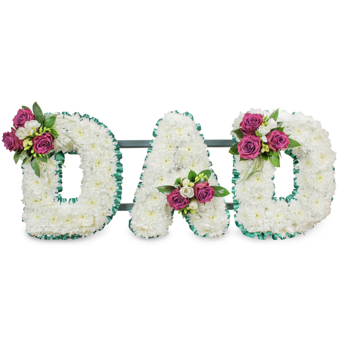 A carefully composed sympathy tribute photographed on a plain white background, the arrangement spells out DAD in generous, three-dimensional capital letters made from densely packed white chrysanthemums. The tiny, feathery heads of the chrysanthemums form a continuous, soft-textured surface that reads as peaceful and pure. Each letter's profile is neatly edged with a ruffled emerald-green ribbon that follows both outer and inner lines, offering a crisp, respectful contrast that highlights the letters' sculptural form. Small, intentional clusters punctuate the design: the first D carries a cluster at its upper left curve, the A holds its bouquet tucked into the lower central V, and the final D is graced on the upper right curve - each cluster composed of deep magenta roses in various stages of opening, interspersed with delicate white freesia and lush dark-green foliage for tonal richness. A discreet dark green or grey horizontal bar behind the letters suggests a secure stand, prepared for display at a chapel or graveside. The arrangement's scent and texture are gentle - the chrysanthemum's soft, almost chalky scent softened by the sweeter rose perfume and the fresh greens. As crafted by Flowers Golders Green for families across the area, this piece balances classic dignity with intimate warmth, a fitting floral statement for a funeral service near Golders Hill Park or a memorial in the heart of Golders Green.