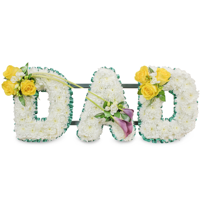 A striking, dignified tribute crafted to read from a distance, the word DAD stands in large, voluminous letters made entirely from pristine white spray chrysanthemums, their small heads packed tightly to form soft, rounded surfaces. Each letter is given a tailored boundary with a ruffled dark green satin ribbon that creates a bold contrast and a refined frame; the ribbon's texture catches the light differently than the blooms, adding subtle depth. Behind the letters, narrow dark green metal support bars run horizontally, visible in the negative space and reassuringly suggesting solidity and cohesion. The arrangement sits against a clean white background so every petal and ribbon fold is clearly legible. Accents are placed to speak in colour and feeling. On the left D a radiant grouping of sunny yellow roses-three to four full blooms-sits on the upper left curve with delicate white filler flowers like freesias or gypsophila and fresh green leaves; two elegant, bare green stems extend diagonally toward the centre, introducing movement. The centre A is adorned low on its left leg by two deep purple or burgundy calla lilies; their slender, trumpet-shaped forms lend a refined stillness, surrounded by tiny white accents and glossy foliage. The right D mirrors the left, providing visual symmetry and comfort. The scent is quietly floral-clean freesia and soft rose-evoking bright afternoons and remembered laughter. Appropriate for memorials at local sites from Golders Green crematorium to small family gatherings in Hampstead Garden Suburb, this bespoke piece balances tranquil white, warm yellow, and reverent purple in an elegant farewell to a father.