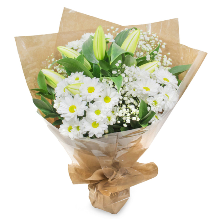 A thoughtfully arranged bouquet of white and green flowers is shown standing upright against a pure white background, as if just finished on the workbench of a local Golders Green florist. The primary impression is of softness and light, created by an abundance of daisy-like white chrysanthemums whose delicately layered petals form gentle domes around vivid yellow-green centres. These centres, neither harsh yellow nor dull green, glow with a subtle energy that prevents the design from ever feeling flat or cold. Rising among the daisies are several sleek lily buds, their long forms tapering to closed tips that are brushed with fresh pale green, the petals still tucked in, holding back their fragrance for another day. Fine tendrils of gypsophila, or baby's breath, lace throughout the bouquet, their tiny white blooms giving a feathery, almost cloud-like lightness between the more solid flowers. Surrounding everything is a collar of lush dark green leaves, smooth and slightly glossy, providing structure and a sense of natural abundance, as if cut fresh from gardens tucked behind the houses off Finchley Road. The stems are neatly bound and wrapped first in rustic brown kraft paper, the paper gently crumpled and folded to create a conical shape that feels both simple and elegant. Over this, a layer of clear cellophane hugs the bouquet, catching soft highlights and readying it for a thoughtful delivery in the Golders Green area. The overall effect is tranquil and reassuring, the kind of sympathy or get-well bouquet that quietly fills a room with a feeling of care, dignity, and hope without ever demanding attention.