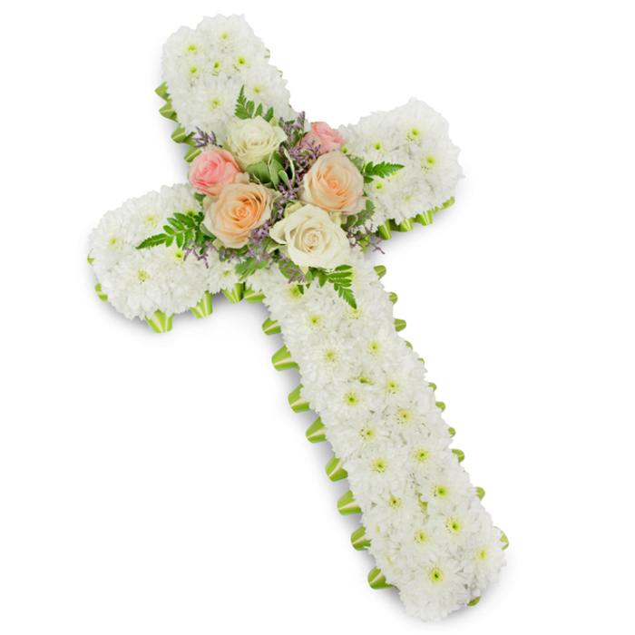 A reverent memorial cross, meticulously assembled from dense clusters of small white chrysanthemums, presents a serene and tactile statement against a pristine white backdrop. Each button-style chrysanthemum is positioned to create a uniformly soft, almost velvety surface across the full cross, the compact arrangement evoking purity, innocence and solemn calm. At the heart of the design a refined spray of premium roses takes the focal point - fully open blooms in creamy ivory, soft blush pink and warm apricot-peach arranged with attentive balance. Interlaced green fern fronds lend natural structure and a touch of graceful movement, while tiny lavender or pale purple filler blossoms introduce a delicate colour contrast that reads as gentle and respectful rather than celebratory. A narrow lime-green ribbon traces the outside edge of the cross, neatly defining its silhouette and offering a subtle, modern edge against the dominant white. The composition's three-dimensional presence is enhanced by a soft drop shadow on the white surface beneath, which underscores the craftsmanship and scale. As a local florist serving Golders Green and nearby streets like Hoop Lane and Finchley Road, Flowers Golders Green often prepares this style of tribute for services at Golders Green Crematorium or family-led memorials in the area - an arrangement designed to convey reverence, comfort and enduring affection during bereavement, created with precise floral technique and thoughtful, compassionate intention.