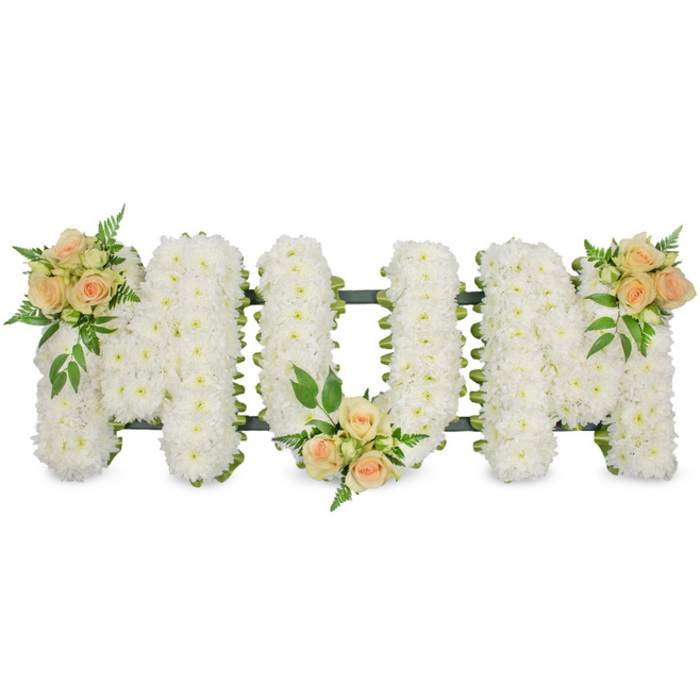 This photograph shows a lovingly crafted funeral tribute where the word MUM is spelled out in three generously sized capital letters, set crisply against a bright white studio background. The letters themselves are expertly built from a dense bed of white spray chrysanthemums, each tiny flower head contributing to a rich, plush surface that looks soft enough to rest a hand upon. Their clean white petals symbolise purity and peace, and they are so closely woven together that the eye reads the word instantly, even from a distance. Around the edges of the letters, a narrow dark green frame or ribbon peeks through, giving the tribute structure and a subtle contrast, much like the greenery that edges the residential gardens around Golders Green. To add warmth and a gentle focal point, the florist has arranged three clusters of roses in soft peach and blush pink tones. One sits confidently on the upper left section of the first M, another nestles in the lower central curve of the U, and the final cluster rests on the upper right of the second M, creating an elegant diagonal flow. The roses themselves are at different stages, from tight buds to unfurling blooms, and they are surrounded by a mix of leafy greens and feathery fern fronds that introduce a natural, airy texture. The tribute feels both dignified and intimate, ideally suited for a mother's funeral or memorial service in the Golders Green area. It is easy to imagine this piece being delivered by Flowers Golders Green to a local chapel, crematorium, or family home, forming a central part of the floral display that honours a loved one's life.