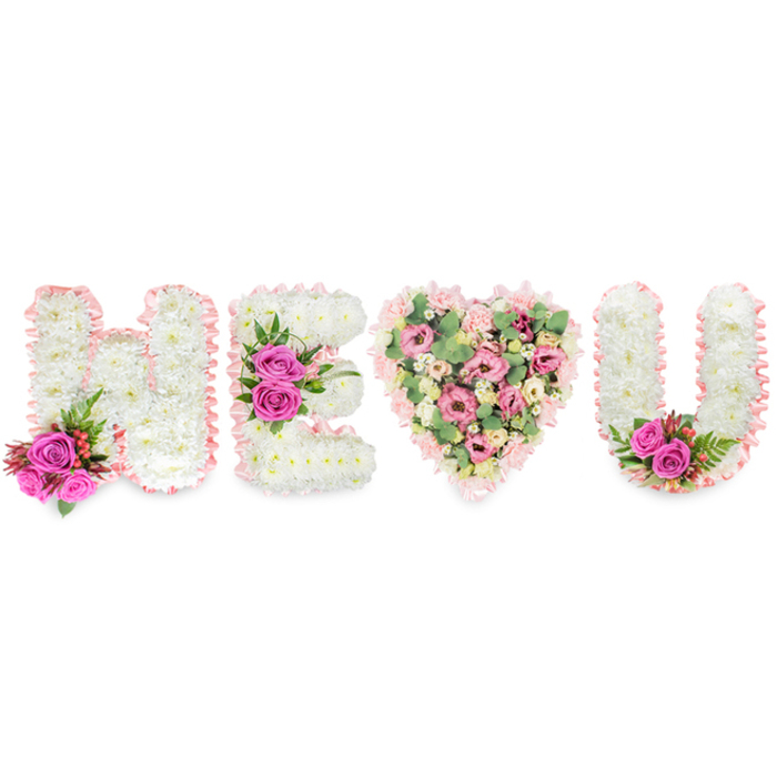 A visually composed message of love and remembrance takes shape here as H E (heart) U, photographed against a brilliant white surface that emphasizes form and colour. The three letters are expertly made from concentrated beds of white chrysanthemums, each bloom snug against its neighbour to form seamless, tactile letters whose surfaces appear soft to the touch. A delicate blush-pink satin ribbon borders each letter with a subtle pleat that catches light and suggests a ribboned keepsake. Strategic accents of fuchsia roses - vivid, velvety and rich - anchor the letters: a pair at the foot of the H, a focal triplet along the E's mid-bar, and two roses brightening the inner curve of the U, each supported by dark green foliage and small red berries that add a classical, sombre punctuation.
The heart at the centre switches to a gentler palette: layered pale pink carnations, cream-tinged lisianthus and petite blush roses are woven with soft eucalyptus leaves, creating a romantic, fragrant centrepiece. The varied textures - the fluffy chrysanthemums, the ruffled carnations, the silky ribbons and the waxy eucalyptus - invite both sight and touch, while the arrangement's mood spans tender affection and dignified remembrance. As a florist who delivers across Golders Green and nearby Hampstead Garden Suburb, I picture this piece placed with care at a celebration of life or as a cherished tribute for those gathering near Finchley Road or at family services in the neighbourhood.