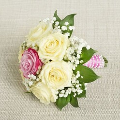 This tender, bridal-inspired bouquet, artfully arranged by experienced Golders Green florists, finds harmony between classic elegance and modern joy. The composition features a circle of large, creamy white roses, their petals opening with a graceful sense of expectation-symbols of new love and cherished beginnings. Offset amid this pale harmony sits a single magenta rose, strikingly vivid, its hue echoing the blooming rhododendrons seen in early summer at Golders Hill Park. Gentle sprays of white baby's breath weave throughout, adding a natural lightness reminiscent of morning mist over Hampstead Heath. Deep green leaves-sleek and glossy-peek through the arrangement, grounding the soft palette with a flourish of freshness. The bouquet's handle is tightly wrapped in bright pink satin ribbon, and the addition of a spiral of tiny white pearls lends a delicate glint of celebration to the piece. This bouquet, resting on neutral linen, radiates a sense of calm and anticipation-imagine the soft scent of roses mingling with nearby greenery as the celebration unfolds on a quiet Golders Green street. Perfect for intimate weddings, bridal showers, or special anniversaries, the bouquet reflects thoughtful craftsmanship, a gentle fragrance, and the easy sophistication that defines both the flowers and their North London surroundings. Each element, from bold blooms to classic adornments, speaks to the artistry and warmth of local florists dedicated to marking life's most poignant occasions.