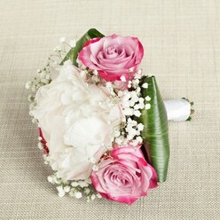 Imagine a bouquet crafted by an experienced Golders Green florist-compact and enchanting, perfectly suited for a wedding or heartfelt celebration. At its core, two radiant pink roses unfold with a gradient from bold fuchsia edges to serene blush pink and soft lavender near the centre, their freshness echoing the early spring blossoms seen along Finchley Road. Between them, a magnificent white peony sits at full bloom, its countless ruffled petals forming a creamy, luxurious core. Wisps of baby's breath dance throughout, scattering clusters of dainty white, reminiscent of clouds drifting above Golders Hill. Broad, glossy green leaves form a structured base, folded with skill to embrace and accentuate the vivid florals, while a soft white satin ribbon wraps the stems elegantly and comfortably for carrying through Golders Green's leafy lanes or into Hampstead Garden Suburb's historic settings. The bouquet's gentle aromas and softest hues conjure feelings of romance, joy, and new beginnings-each detail highlighted by diffuse natural light, inviting admiration for its precision and grace. Whether for a bridesmaid, a bride, or as a loving gift, this hand-tied arrangement brings a touch of Golders Green's timeless beauty to life's cherished moments.