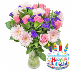 Captured in soft, natural light against a clean white backdrop, this joyful birthday arrangement blends romantic pinks with lively purples and glossy foliage. At the heart of the design are numerous soft-pink roses, their petals layered and slightly cupped, graduating from pale blush at the edges to a richer rose-pink toward the centers, evoking warmth and affectionate sentiment. Pale pink Gerbera daisies sit among the roses, their broad petals forming cheerful discs with pale, buttery centres that lift the composition with a touch of classic charm. The bouquet's texture is enlivened by abundant clumps of deep purple statice or limonium, which provide crisp, papery contrast and a three-dimensional ripple throughout the mass of blooms. Healthy, deep green leaves frame and support the flowers, their glossy surfaces catching the light and reinforcing the fresh, just-arrived-from-the-market feel. Arranged in a simple, clear glass vase filled with water, the visible stems suggest careful preparation by an experienced florist. To the right, a cake-shaped foil balloon decorated with white 'icing,' a blue scalloped border, colorful sprinkles and four multi-coloured candles proclaims Happy Birthday in playful, bright letters, while a small KALEIDOSCOPE logo sits at the bottom edge. The image reads as a complete birthday gift-visually balanced, fragrant in imagination, and perfect for delivery to a Golders Green home or for pickup on Golders Green Road or near Golders Hill Park when you want to combine classic floristry with a fun celebratory accent.