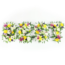 Presented flat against a clean white background and lit with steady daylight-equivalent lighting, this bespoke floral tribute spells BEST in four bold, letter-shaped panels, each lovingly constructed from dense clusters of fresh blooms and rich foliage. The dominant palette is crisp white and cheerful yellow: plush white chrysanthemum-like blooms and ivory gerberas create a serene base while bright yellow roses and gerbera daisies bring a sunlit warmth. Interspersed are gentle lavender and deeper purple lisianthus or similar small chrysanthemums that lend quiet dignity, and vivid fuchsia-pink spray roses or carnations provide lively accents. Tiny green and white filler blossoms give tactile interest and help the letters hold a soft, sculpted surface, while generous fern fronds cradle each form with deep, glossy green, creating a natural border. A discreet dark-green or grey metal armature shows through in places - particularly across the middle bar of the 'E' and the top of the 'T' - revealing the experienced construction beneath the floral sweep. The overall effect is calm but uplifting, a carefully balanced piece that speaks of honour and fond remembrance. As Flowers Golders Green would arrange for families in the area, this composition is suitable for funeral services at nearby Golders Green Crematorium or for a memorial tribute laid at a local synagogue, conveying love and respect through handcrafted floristry. The scent is quietly floral and comforting, and the design is sized for easy transport and local delivery around Golders Green and Finchley Road.