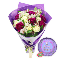 Set against a clean white background, a lovingly arranged bouquet and coordinating balloon form a romantic still life that feels ideal for couples celebrating in Golders Green. The bouquet is full and rounded, composed of creamy white roses with neatly furled centres, their petals soft and luminous as if freshly opened that morning. Between them, clusters of deep magenta and burgundy carnations lend depth and drama, their layered, frilled petals giving a tactile, almost cushiony richness. Threaded amongst the larger blooms, white alstroemeria unfurl slender petals marked by fine reddish-brown streaks, a delicate pattern that draws the eye in closer, much like spotting the first blossoms on a quiet walk through nearby Golders Hill Park. Surrounding the flowers, fresh green foliage and hints of variegated leaves add structure and movement, suggesting a bouquet shaped carefully by an experienced local florist's hand. The stems are wrapped in a smart two-layer finish: a smooth white paper that supports the design, overlaid with sheer, crinkled purple cellophane which rises above the blooms in soft, translucent folds, catching the light like silk. A slim bright green satin ribbon cinches the base, tied in a petite bow with a small light brown gift tag ready for a personal dedication from one partner to another. Resting to the right side is a metallic purple foil balloon, round with a scalloped, rosette-style edge, echoing the celebratory mood. In its lighter purple centre panel, the message "To Loving Partners" is written in graceful pink script, accompanied by a jagged rainbow holographic sticker that hints at playful sparkle. Together, this floral and balloon pairing encapsulates affection, commitment, and quiet celebration, perfect for anniversaries, date nights at home, or romantic gestures delivered across NW11.