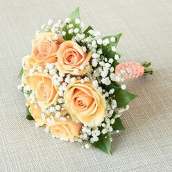 Lying gracefully atop a softly woven linen surface, this beautifully crafted bouquet captures the romantic spirit of Golders Green. Homegrown expertise shines through in the arrangement-a harmonious round cluster of seven to eight peach-tinged roses, their petals tenderly curling outward from tight spirals, each bloom bathing in hues from pale apricot to soft sunlit orange. Delicate clouds of baby's breath are carefully threaded between the roses, lending the whole bouquet an ethereal, floating lightness that brings to mind early mornings along Golders Green Road or the gentle hush of Childs Hill. Rich green foliage emerges subtly from under the blooms, infusing depth and balance, reminiscent of the refreshing greenery found around Golders Green's famed parks. A flawlessly wrapped coral-peach ribbon secures the bouquet's stems, its sheen catching the light, while a dreamy swirl of tiny white faux pearls adds textural interest-a nod to wedding-day elegance and cherished local traditions. At the base, the fresh stems peek through, promising enduring vitality and connection to the season. From its gentle colours to its cloud-soft accents, this bouquet is a perfect accompaniment for an intimate Golders Green celebration, radiating feelings of joy, anticipation, and the enduring artistry only a local florist can infuse into every petal.