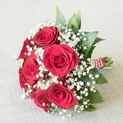 Crafted with discerning artistry by a Golders Green floral specialist, this hand-tied bouquet makes for a breathtaking visual centrepiece-perfect against the textured off-white canvas of a fine London home. At the forefront, lush red roses dramatically unfold, their petals rich in velvety depth and layered to form exquisite spirals that evoke sentiments of unwavering romance. Bleached-white clouds of baby's breath float among the roses, offering an artful contrast with a feathery touch, much like the gentle late-spring sunlight gracing Golders Green's quiet corners. Interspersed glossy green leaves add vitality, reminiscent of the local parks and gardens that shape the character of the neighbourhood. At the bouquet's base, sturdy stems are masterfully woven together with an eye-catching ribbon in red and white, thoughtfully accented by a strand of small, radiant pearls-a finishing accent rooted in traditional bridal elegance. The bouquet is set naturally yet purposefully against a soft background, letting the saturated hues and intricate details take centre stage. Ideal for weddings held in Golders Green's charming synagogues or celebrations along Finchley Road, this romantic arrangement whispers of lifelong promises, joyful nuptials, and the quiet anticipation of new beginnings. Each facet-from the fragrance of fresh-cut roses to the glimmer of pearls-reflects the cultivated expertise and heartfelt passion of local florists.