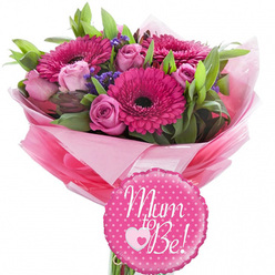 Set against a clean, uncluttered white background, this celebratory maternity bouquet appears as if it has just been lifted from a local Golders Green florist's bench, ready to delight an expectant mother. Bold fuchsia gerbera daisies form the main focal points, their rich pink petals radiating from deep, contrasting centres that draw the gaze inward. Between them, softly blushed pink roses in different stages of bloom suggest a story unfolding-some petals still tightly wrapped, others opening in delicate spirals that feel almost silk-like in the imagination. Weaving between the larger blooms are sprigs of tiny purple filler flowers, adding light texture and a hint of countryside charm, reminiscent of wildflowers gathered on a stroll through nearby Golders Hill Park. Surrounding the flowers, fresh green foliage in slender and broader leaves provides a cool backdrop, giving the arrangement fullness and a sense of natural movement. The stems are gathered and wrapped in layers of pink tissue paper, from bright raspberry tones to paler blush shades, then finished with a layer of clear, glossy cellophane that catches the light and emphasises the gift-like presentation. At the front, a round, bright pink foil balloon with a scalloped edge and crisp white polka dots adds a playful accent. Across its centre, the words "Mum to Be!" are written in flowing white script, with a sweet heart detail nestled in the message, capturing both joy and tenderness. The overall impression is of a thoughtfully crafted baby shower bouquet, perfect for same-day delivery in and around Golders Green to celebrate new beginnings and share heartfelt good wishes.