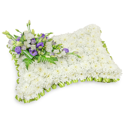 A carefully composed sympathy pillow, lovingly assembled by local hands, rests on a bright white field that accentuates its pure, restorative tones. The central surface is a thick carpet of immaculate white chrysanthemums, each head placed close to its neighbor to form a seamless, plush texture that invites the eye to linger. The pillow's gentle rectangular silhouette, with rounded edges and a mild puffiness, evokes a sense of rest and protection; soft shadows beneath suggest a tender weight and dimensionality. Encircling the piece, a soft, light green ribbon has been pleated into consistent loops, the fresh color offering a subtle springlike contrast to the sea of white and framing the tribute with quiet grace. Nestled in the top-left quadrant, a small, elegant cluster of flowers gives the design a private voice: crisp white lisianthus mingle with rich purple lisianthus - some opening, some in tight bud - while delicate fern fronds and broad dark leaves provide texture and an evergreen calm. A darker green leaf wrap binds the stems, visible and neat, like the finishing touch of an experienced florist. The arrangement carries a delicate floral scent and a contemplative energy, made to console at memorials, wakes, or graveside services around Golders Green Road, Finchley Road, and the surrounding neighbourhoods. Created with local care by Flowers Golders Green, it reads as both a formal tribute and a personal farewell.