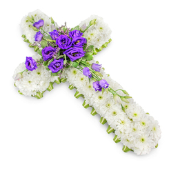 A traditional Christian cross of flowers is pictured resting on a clean white backdrop, its form both simple and profoundly moving. The entire structure is built from a tightly woven blanket of small white chrysanthemums, each bloom fresh and immaculate, forming a smooth, cushiony surface that looks soft to the touch. Their uniform white petals and subtle green eyes create a sense of order and calm, symbolising purity and peace. Around the outer edge, a narrow trim of bright lime-green ribbon carefully follows the contours of the cross, defining its outline and adding a modern, uplifting note of colour without disturbing the solemn character of the design. At the very heart of the cross, where the arms meet, the chrysanthemums give way to a striking cluster of rich purple lisianthus flowers. Their ruffled, bell-shaped petals unfold in varying shades of violet and royal purple, standing out vividly against the white field like a focal point of reverence and hope. Delicate sprigs of soft green foliage and a few unopened buds are tucked among the lisianthus, giving depth and a gentle sense of movement. From this central gathering, several lisianthus blooms and buds extend along the lower-right arm of the cross, forming a graceful diagonal line that leads the eye downward. Soft, even lighting casts a faint shadow beneath the tribute, enhancing its three-dimensional presence without breaking the serene mood. This floral cross, the kind of arrangement often chosen for memorial services in churches near Golders Green High Road or quiet farewells at crematoria in the surrounding area, is a heartfelt expression of sympathy and remembrance, crafted to bring comfort to grieving families.