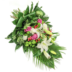 This elegant diagonal floral spray, set against a pure white background, exudes calm reflection and refined artistry-an arrangement reminiscent of peaceful walks through Golders Green's tree-lined avenues. At its heart, fragrant white lilies unfurl alongside budded counterparts, their trumpet-shaped blooms radiating serenity and purity. Interspersed throughout are fuchsia and deep pink roses, their soft petals suggestive of cherished memories-each flower a warm reminder of Golders Green's welcoming spirit, from Childs Hill to the quiet corners near Golders Green Crematorium. Vibrant green, button-shaped santini chrysanthemums lend a playful, modern counterpoint, their mossy texture enlivening the ensemble. Smaller, ruffled white carnations nestle between blooms, lending layers of softness and comfort. Glossy red hypericum berries are scattered like jewels among the flowers, offering bright pinpoints of contrast against generous waves of varied green foliage. The greenery ranges from dark, broad leaves-some neatly folded-to delicate, lighter fronds, building depth and natural movement, anchored by the sophisticated downward sweep of slender palm leaves. Subtle natural lighting highlights the interplay of texture and hue, making each bloom sing with fresh vitality. This arrangement, thoughtfully composed by skilled local hands, brings solace and admiration to occasions of remembrance, gently offering Golders Green families a heartfelt tribute filled with grace and peaceful beauty.