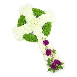 A full, flower-covered Celtic cross tribute is displayed diagonally across a bright white background, as though gently laid down for a moment of contemplation. The base of the cross is packed with countless white chrysanthemum blooms, their petals forming a plush, cloud-like surface that softens the strong geometry of the shape. Tracing through this field of white is a precise network of lime green button chrysanthemums, arranged in a ring and interlocking bands that echo traditional Celtic knotwork, giving the design a sense of heritage and timeless symbolism. The green flowers sit slightly raised, catching the light and adding intricate texture to the cross, almost like living stonework carved from fresh foliage. On the lower length of the cross, three distinct groupings of deep magenta-purple carnations create a moving focal point. Their rich colour and frilled petals suggest both tenderness and depth of feeling, while fine strands of dark greenery and slender, wiry stems weave around them, softening the edges and giving the piece an organic, garden-like touch. The lighting is clean and even, showcasing each flower head and the craftsmanship behind their placement, as if prepared by an experienced Golders Green florist used to guiding families through moments of loss. It is easy to imagine this floral cross being delivered to a funeral service or memorial gathering off Finchley Road or near Golders Green Crematorium, where the blend of white, green, and purple would quietly convey sympathy, respect, and spiritual comfort. The tribute feels serene and contemplative, a carefully made symbol of faith and remembrance.