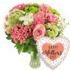 This image shows a luxurious Mother's Day flower and balloon gift set, styled as a clean product photograph on a bright white background, much like the displays you might see in a Golders Green flower shop before morning deliveries go out. A clear glass vase holds a lush, domed bouquet overflowing with fresh blooms in pink, coral, lime green and white. The eye is drawn first to several generous pink roses, whose petals deepen in colour toward the centre and soften to paler edges, suggesting tenderness and affection. Threaded around them are clusters of tiny coral-pink blossoms, similar to kalanchoe, forming dense, starry heads that bring texture and a slightly modern twist. Lime-green button chrysanthemums and velvety chartreuse florets create a playful contrast, their rounded forms and frilly surfaces echoing the lively character of nearby Golders Hill Park in spring. Between these sit delicate white daisy-like spray chrysanthemums and a few smaller, spiky coral blooms, giving the arrangement a light, airy movement. Dark green foliage cups the flowers and spills gently outward, grounding the brighter tones and framing the composition. The stems, neatly cut and immersed in clear water, are visible through the transparent vase, reinforcing the sense of just-picked freshness, perfect for same-day delivery around NW11. To the lower right, a shiny heart-shaped foil balloon completes the gift. Its white surface is dotted with irregular spots of gold, silver and soft peach, and at the centre a bold peach-coral heart bears the message "HAPPY Mother's DAY" in stylish black lettering. The overall mood is celebratory yet heartfelt, capturing the feeling of bringing a smile to a mum's face in Golders Green, Temple Fortune or along Finchley Road on Mother's Day.