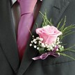 There's a quiet poetry to this expertly crafted buttonhole, echoing both the romance and vibrancy of a Golders Green celebration. At the centre, a blush-pink rose-petals unfolding softly, like the first light of day-sets an intimate, enchanting tone. The delicate scent of the fresh rose, thoughtfully sourced from a local florist, sparks a sense of new beginnings perfectly suited for wedding vows or prom night. Surrounding the rose are airy tufts of white baby's breath, their lightweight blossoms adding an ethereal softness that enhances the rose's tender glow. Fanning behind are slender ribbons of green foliage, which arc with easy grace to conjure the lush greenery found in nearby Golders Hill Park. A deep lilac satin ribbon at the base matches the accompanying tie, offering a hint of shimmer that lends playfulness and unity to the ensemble. Resting against a sharp charcoal lapel and complemented by a vibrant fuchsia tie, the boutonniere glows with understated confidence and artistry-an ideal finishing touch for life's most cherished moments, crafted with heart in the very heart of Golders Green.