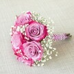 A vibrant round bouquet, designed with care in Golders Green, bursts with five lush fuchsia and lavender roses-each flower opening gracefully to reveal a dynamic two-toned blend of gentle purple merging into bold magenta along the petal edges. The roses are thoughtfully interlaced with airy white baby's breath, creating a soft, cloudlike harmony that both highlights and cradles the radiant blooms. The hand-tied stems are cloaked in a textured plum satin ribbon, its surface glimmering subtly and spiral-wrapped with lustrous pearl strands for a refined, contemporary finish inspired by the local artisan spirit. At the bouquet's base, freshly cut green stems peek out, a subtle nod to freshness and authenticity. Laid diagonally upon a gentle beige linen fabric that recalls the chic simplicity of Golders Green cafés, the arrangement's rich colours and intricate details stand out brilliantly under soft afternoon light. Elegant and joyful, this bouquet is perfect for a Golders Green wedding, bridesmaid, or special romantic celebration-a symbol of local creativity, love, and new beginnings, delivered with heartfelt care to homes and venues throughout NW11.