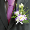 Pinned above the heart on a dark, well-cut jacket, this boutonnière combines classic refinement with a crisp, contemporary twist-a small composition that speaks louder than its size. The central white lisianthus, edged in a striking violet-purple, opens like a quietly radiant star, its velvety layers catching soft light. Complementing it is a compact dianthus with white petals ruffled in lively purple, introducing a playful textural contrast. Wisps of gypsophila lace the arrangement with airy white points, while slim ornamental grasses and deep green foliage arch and cradle the blooms, suggesting movement and new growth. A single spike of deep indigo veronica adds elegant height and an unexpected vertical line, balancing the rounded forms below. Everything is gathered with a crisp white ribbon whose clean fold speaks of careful hands and considered design-details our workshop at Flowers Golders Green attends to daily when preparing pieces for ceremonies along Finchley Road, Hoop Lane and around Golders Hill Park.

Beside a lustrous magenta tie, the boutonnière reads as thoughtful and slightly bold; the materials hold a soft, garden-fresh scent and a subtle tactile richness that invites a gentle touch. It's well suited to weddings, anniversaries and commemorative gatherings in the local community, where small botanical accents carry personal meaning. The overall effect is one of sophistication without fuss-a wearable keepsake that holds tenderness, anticipation and the quiet expertise of a neighbourhood florist.