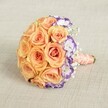 A gracefully composed round bouquet, set in front of a gentle beige background, evokes the elegant spirit of Golders Green celebrations. At the bouquet's center, sumptuous roses bloom in a palette ranging from pale peach to soft apricot and honeyed orange, all packed tightly for a lush, inviting texture that feels both plush and romantic. Along one arc, ruffled lisianthus blossoms add flair-white petals edged dramatically in purple, their playful tones bringing to mind springtime strolls in Golders Hill Park. Wispy strands of baby's breath hover delicately within, their tiny white blooms infusing the arrangement with a dreamy, ethereal lightness. The stems are securely hand-tied with a luxurious peach satin ribbon, cool and satiny against the skin, while a string of pearls, finely wound, gives the base a refined, traditional accent-a hallmark of local wedding bouquets in this friendly North London neighbourhood. Perfectly balanced between classic charm and contemporary design, this bouquet is an ideal choice for brides, anniversary celebrations, or luxury gifts delivered across Golders Green and its leafy surrounds. Its harmonious colours, intricate detail, and romantic air ensure it will be remembered long after the celebration ends.
