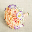 Captured on a textured, light-beige fabric that resembles linen, this bridal-style bouquet centres on a cluster of plush peach-apricot roses whose petals curl inward before opening into soft, layered spirals. The roses' warm, sunrise tones are brightened by ruffled white lisianthus, each edged with a vivid violet-purple halo that frames the blooms like delicate brushstrokes. Scattered throughout are tiny sprigs of baby's breath, their cloudlike white flowers creating a feathered softness that fills negative space without stealing the spotlight. The stem-wrap is a pale blush-peach ribbon, meticulously wound and decorated with several rows of small, lustrous cream pearls that catch the light and add a refined, tactile finish. At the base, neatly trimmed green stems provide a fresh, living contrast to the ribboned handle. Soft, even lighting reveals the sheen of petals and the fine textures of the blooms, while a subtle suggestion of sweet rose fragrance mingles with green stem notes. The colour palette - warm peaches, clean whites, and cool purples - reads romantic and sophisticated, suitable as a bridal bouquet or a milestone gift. As a local florist serving Golders Green and neighbouring Hampstead Garden Suburb, Flowers Golders Green arranges these blends of texture and tone with care, and the bouquet pictured is ideal for ceremonies held near Golders Hill Park or small celebrations on Golders Green Road.