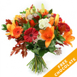 A hand-tied autumn bouquet captured against a pristine white backdrop, the composition warm and generous as a crisp Golders Green morning. At its heart sit wide, trumpet-shaped orange lilies, their open petals and prominent stamens forming an immediate focal point; a few still-closed lily buds promise more bloom in the days ahead. Scattered among them are cheerful Gerbera daisies in deep red and vivid orange, their concentric petals catching the light and smiling outward. Soft, ruffled white Lisianthus provide a cool, creamy counterpoint, their delicate edges easing the arrangement's richness. Small, star-like Astrantia with purple-pink centres add an intricate, almost lacy texture that invites close inspection. The flowers rest on a bed of lush, dark green foliage-ruscus or salal-whose glossy leaves lend density and a verdant frame. Most notable are the deeply lobed oak leaves tucked through the bouquet: burnt orange and deep reddish-brown, they give the design an unmistakable autumn voice and a hint of woodland. The stems are gathered and tied in simple dark twine, finishing the piece with a rustic, hand-made feel. Lighting is soft and even, so the colours read true and the textures-silky petals, papery oak leaves, glossy greens-are easy to imagine. In the lower right corner a bright diagonal orange banner overlays the image, boldly stating FREE CHOCOLATE in white letters, a visual cue to a seasonal add-on for customers considering flower delivery. As a local florist might say, this bouquet brings the tactile comfort of fall-scent, colour and memory-perfect for welcoming autumn, sending thanks, or brightening a friend's door in Golders Green.