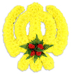 A reverent, handcrafted floral Khanda fills the frame: the Sikh emblem sculpted entirely from thousands of small, bright yellow chrysanthemum heads, densely packed to create the emblem's circular chakkar, the upright double-edged khanda and the two crossed kirpans beneath it. The yellow surface reads as soft yet sculpted, petals layered like fine textile, catching a cool, even studio light that makes the sunny tones glow against a pure white background. At the geometric centre, five deep red roses are arranged in a compact cluster and cushioned by rich, dark green fern fronds, their serrated textures offering a fresh, leafy counterpoint to the round, velvety rose buds. A faint grey shadow beneath the tribute gives the piece subtle depth and confirms it as a physical ceremonial wreath or freestanding memorial emblem. The scent, if one could imagine it, would be a gentle wash of sweet chrysanthemums brightened by the warm, classic perfume of red roses and the green, slightly earthy note of ferns. Crafted with the careful hand of an experienced florist who understands Sikh symbolism, this composition reads as both traditional and contemporary: the bright yellow conveys remembrance and hope, while the concentrated red at the heart speaks of respect and enduring love. Suitable for religious ceremonies, memorials at local spaces such as Golders Green Crematorium, or cultural commemorations near Golders Green tube, the arrangement is photographed simply to emphasise craftsmanship, colour contrast and the spiritual significance inherent in the Khanda form.