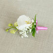 A refined wedding boutonniere rests gracefully on a natural, oatmeal-coloured linen surface, the softly woven texture of the fabric forming a calm, neutral backdrop for the floral artistry. At the centre sits a pristine white Phalaenopsis orchid, its petals wide, smooth, and gently undulating at the edges, like layers of silk laid one atop another. Light seems to skim across the orchid's surface, catching the delicate curves and leading the gaze into its intricate throat, where a wash of yellow-orange and a whisper of pink lend a warm, romantic glow. Encircling the orchid, fine sprays of Gypsophila, or baby's breath, create a cloud of tiny white dots, their clustered blossoms and threadlike stems softening the overall silhouette and lending an almost ethereal quality. A few slender green leaves are tucked strategically around the bloom, their fresh colour and clean lines giving subtle structure and a lively contrast. Extending thoughtfully to one side, a stem carries three rounded, pale green orchid buds, still closed, hinting at beauty yet to open and echoing the feeling of new beginnings that weddings and proms in Golders Green, Hampstead Garden Suburb, and the surrounding streets often carry. The stem of the boutonniere is wrapped in lustrous bright pink satin ribbon, the material smooth and reflective, tied in a neat, compact bow with short, elegant tails that rest against the linen. The overall composition suggests calm confidence and intimate celebration, the kind of handcrafted detail a careful florist would create for a groom or guest preparing for a special day in North West London's elegant venues and synagogues near Golders Green Road.