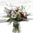 A visual symphony, this bouquet harmoniously melds deep red roses with creamy white gerberas, each flower hand-selected to reflect the refined beauty of Golders Green's vibrant, leafy neighbourhood. The red velvety roses are bold and expressive, while the white gerberas rest beside them, their petals bright and soft with prominent brown eyes at the center. Pops of pale lilac lisianthus weave playfully through the arrangement, their silhouette suggestive of early morning mist over Golders Hill Park, blending both grace and understated luxury. Silver-green eucalyptus branches stretch outward, their aromatic discs catching the changing afternoon light like the shadows cast by local sycamore trees. The base is gently cupped by robust, glossy green leaves, completing the bouquet's silhouette and adding to its visual weight and sense of abundance. Nestled among the main blooms, clusters of light, fluffy white filler flowers lend a texture as delicate and inviting as freshly baked challah at a Brent Cross café. The clean, clear glass vase not only grounds the display but also allows the vibrant green stems to be seen in pure water, affirming freshness and longevity. Designed to mark moments of gratitude or heartfelt occasions, this arrangement showcases the talent of Golders Green florists, perfectly balancing artistic flair with the welcoming spirit of the area.