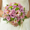 In this photograph, a romantic bridal bouquet appears as though it has just been finished by an experienced florist in Golders Green, the stems still cooling from their final trim. Soft, dusky mauve and lilac roses form a gentle focal point, their spiralled centres opening slowly like a calm breath before saying I do. Around them, pink alstroemerias extend in graceful arcs, their slender petals and darker freckles creating a sense of movement, as if the bouquet itself is mid-twirl on a dance floor near Golders Green Road. Bright green button chrysanthemums sit playfully among the pastels, their round, textured faces adding both freshness and a touch of modernity to the otherwise classic design. Between these bolder blooms, wisps of gypsophila float like tiny white stars, diffusing the transitions between colours and softening every line, much like low morning light drifting through nearby Hampstead Garden Suburb. The foliage is rich and polished, deep green leaves cradling the flowers and creating a natural frame that keeps the eye returning to the roses at the centre. You can almost sense the cool, faintly sweet scent rising from the bouquet, with the roses' softness balanced by the crisp green note of chrysanthemums. The arrangement is captured in tender, natural light, highlighting every petal edge and giving the impression of dew still clinging from an early delivery. Designed for a wedding, engagement, or special celebration in or around Golders Green, this bouquet speaks of trust, partnership, and joyful beginnings, every bloom positioned with the quiet assurance of a florist who understands both tradition and the tastes of local couples.