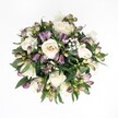 A top-down view of a lush, circular bouquet rests against a bright white background, the clean surface making every blossom stand out with painterly clarity. At the heart of the arrangement, creamy white roses unfold in spirals, their petals moving from soft ivory to pale champagne, some fully open and plush, others still gently cupped as if just beginning to share their fragrance. Nestled between the roses are clusters of Peruvian lily (alstroemeria) buds in deep lavender, rich purple, and dusky magenta, their tips fading into fresh green at the base, adding a sense of movement and youthful energy. Fine sprays of white gypsophila float like a delicate mist throughout, softening the contrasts and bringing a light, romantic air to the design. Dark green, glossy foliage frames and supports the flowers, curving around the outer edge and peeking through the gaps, giving depth and a natural, garden-like feel. The soft, even lighting-similar to calm daylight over Golders Green's quiet residential streets-casts no harsh shadows, instead highlighting each petal's texture and each leaf's subtle sheen. The bouquet feels both refined and inviting, suitable for an intimate anniversary dinner in a Golders Green flat, a thoughtful thank-you for a neighbour near Hampstead Garden Suburb, or a comforting gesture delivered to a friend resting after a walk on Golders Hill Park. The overall mood is serene and elegant, capturing that quiet moment when fresh flowers are first laid out on the workbench, carefully composed by a local florist who understands how to balance classic white roses with contemporary purple accents in a harmonious, timeless display.