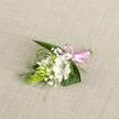 A delicately handcrafted boutonniere rests on a softly textured, light beige linen-style cloth, the neutral background allowing every detail of the flowers and foliage to stand out with quiet clarity. At the heart of the design is a single white alstroemeria bloom, its broad petals gently opening to reveal fine reddish-brown speckles that draw the eye towards the throat of the flower. The petals look almost silky, catching the even, natural light in subtle highlights that suggest freshness and careful handling. Tucked just to the side sits a compact column of vivid lime-green buds, reminiscent of an Ornithogalum or ginger-like spike, each tiny bud tightly packed and giving the piece a sculptural, contemporary twist. Wisps and clusters of classic white baby's breath weave through the arrangement, their tiny cloud-like blossoms softening the stronger shapes and adding a romantic, almost whisper-light texture. Around the flowers, a foundation of deep green, pointed leaves and slender strands of grass-like greenery curves gently, creating movement and framing the central bloom. At the right edge of the stems, a small pink satin ribbon has been tied into a neat bow, its glossy surface catching the light and bringing a playful, celebratory note to the otherwise calm palette of whites and greens. The boutonniere is photographed from above, with balanced, diffused lighting that reveals every vein in the leaves and every speckled detail in the alstroemeria. It feels like a refined finishing touch for a suit lapel at a Golders Green wedding or prom, the kind of careful floral work often chosen for intimate celebrations near Hampstead Garden Suburb or along Finchley Road, where understated elegance and personal craftsmanship are treasured.