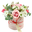 A charming hatbox bouquet in soft pinks, whites, and fresh greens is presented against a clean white background, giving the flowers a spotlight as clear as a bright morning over Golders Green. The container is a smooth, cylindrical box in gentle pastel pink, its matte finish suggesting a luxurious yet understated gift. Around the box runs a slender coral-red satin ribbon, tied into a neat bow at the front, with a cream gift tag hanging delicately from the knot, lettered in green script as if ready to carry a personal message from someone nearby on Golders Green Road.   

The floral arrangement rises above the rim of the box in a graceful dome, lush and rounded, with no harsh angles. A prominent bi-colour rose at the front draws attention: its outer petals are pale blush, gradually deepening to a rich pink swirl at the centre, evoking warmth and romance. Surrounding this focal bloom are clusters of white daisy-like chrysanthemums with bright green centres, their crisp petals bringing clarity and brightness reminiscent of suburban gardens in NW11. Interlaced with them are white alstroemeria, their slender, trumpet-shaped petals carrying delicate speckles inside that add quiet refinement.   

Dotted through the arrangement are smaller flowers in vivid fuchsia and deep pink-perhaps spray roses or lisianthus-that provide lively pops of colour and a playful accent against the softer tones. A generous selection of greenery, including rounded silvery eucalyptus leaves and darker foliage, frames the blooms, while tiny green buds lend a sense of freshness and new beginnings. The overall impression is of a thoughtfully curated, modern hatbox gift, perfect for same-day delivery to mark birthdays, anniversaries, or simple gestures of appreciation across Golders Green and neighbouring streets off Finchley Road.