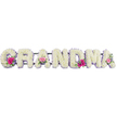 The image presents a gentle, heartfelt funeral arrangement spelling the word GRANDMA in large, individual letters made entirely from white chrysanthemums. Every letter is densely packed with the soft, button-like blooms so that their tiny petals create a smooth, cushiony texture across the surface, evoking comfort and purity. Around the outer edge of each crisp letter runs a fine lilac ribbon, its pale purple tone tracing the shapes with elegance and helping the white chrysanthemums stand out clearly. At three points along the tribute-on the opening G, one of the central As, and the last A-small, carefully composed flower posies provide bursts of warm colour. These clusters combine cheerful pink gerbera daisies with delicate pink roses, the layered petals opening gently over sprigs of fresh greenery. The green leaves and stems peek out to soften the outlines and add a lively, natural feel, like a breath of fresh air drifting across nearby Golders Green Road. The tribute lies on a neutral surface under calm, diffused lighting that highlights the textures without harsh shadows. There are no additional decorations or distractions, allowing the eye to focus on the word GRANDMA and the thoughtful detail in the floristry. The overall impression is one of quiet respect and deep affection-a floral message designed to accompany a final goodbye, perhaps on its way to a funeral service or memorial gathering in Golders Green, Finchley, or the surrounding North London neighbourhoods, expressing love and remembrance through the language of flowers.