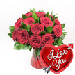 A dramatic, love-filled composition showcases a lush bouquet of deep red roses, paired with a gleaming heart-shaped balloon, all set against a clean white background that makes each colour sing. The bouquet holds roughly a dozen or more roses in a sumptuous, rounded formation, their petals thick and velvety, layered in swirl upon swirl of rich crimson. Some blooms are at their fullest, revealing generous, open faces, while others are just beginning to open, giving the arrangement a sense of life and movement. Surrounding and supporting the flowers, glossy dark green leaves peek between the blooms, their smooth surfaces and deep tones framing the red and creating a striking visual contrast. The stems are gathered in a ruby-red glass vase with soft, fluted lines that run vertically, adding texture and an elegant sense of structure; the glass is translucent, so hints of stems and tinted water can be seen within, contributing to the overall richness. To the lower right, positioned slightly in front of the bouquet, a bright metallic red heart-shaped foil balloon catches the eye. Its surface shines with reflections, and across the heart, the words I Love You are written in bold, flowing white script. A silver Cupid's arrow appears to pierce the balloon diagonally, reinforcing the romantic message. This image feels like a classic Valentine's gift you might send from Flowers Golders Green to a loved one in NW11, perhaps for a surprise delivery to a home near Brent Cross or a cosy apartment off Golders Green Road. The simplicity of the white background ensures that the passion of the reds and the freshness of the greens speak clearly, creating a timeless symbol of love, devotion, and celebration.