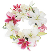 A serene, full circular wreath photographed against a clean white background, composed of large, pure white Oriental-style lilies and vivid fuchsia-pink Stargazer-type lilies, with clusters of pale blush and creamy white roses tucked softly between the larger blooms. The white lilies dominate with broad, star-shaped petals, some fully open to reveal their pale green pistils and subtle yellow stamens while others hover in various stages of bud, giving the wreath a natural, living rhythm. Deep magenta-pink lilies provide dramatic punctuation - speckled toward their throats and curling slightly at their tips - which draws the eye around the unbroken ring. Gentle green foliage, likely eucalyptus and lily leaves, peeks from beneath the flowers, adding muted texture and framing the composition without overpowering the blooms. The wreath's open centre and dense outer garland create a sense of calm completeness, and the overall palette - snow-white, soft blush and rich fuchsia - communicates quiet dignity and warmth. There is a faint suggestion of sweet, honeyed lily perfume and the satiny feel of ruffled rose petals; soft studio lighting highlights the velvety surfaces and delicate veining of each bloom. As a florist's tribute, this arrangement reads as respectful and intimate, suitable for memorial services or moments of condolence, quietly honoring a life with a blend of purity, tenderness and vivid remembrance. The craftsmanship is deliberate, its balance calibrated to comfort viewers and invite reflection rather than spectacle.