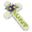 A large, reverent floral cross arrangement is shown laid out flat against a pure white background, its details crisp and easy to distinguish. The entire surface of the cross, from the broad arms to the extended base, is densely filled with pristine white chrysanthemums, each bloom contributing to a smooth, cloud-like texture that feels soft and embracing. This unbroken field of white suggests purity, peace, and a gentle farewell, much like the quiet moments shared with family after a service in one of the chapels around Golders Green. Around the outer edge runs a slim, vivid green border of ribbon or foliage, neatly defining the Christian cross shape and adding a subtle but refreshing hint of colour. Down the centre of the long vertical arm, a panel of lime green button chrysanthemums creates a graceful contrast; their small, perfectly rounded heads form a delicate pattern that draws the eye downward. Fine, pale decorative wires cross over this green section in a light lattice, adding interest and refinement without overpowering the flowers themselves. At the intersection of the arms sits an elegant focal cluster of deep purple lisianthus (Eustoma), bright lime green chrysanthemums, and airy sprigs of fern. The lisianthus petals curl in gentle layers, their velvety purple tones rich and contemplative, while the lime accents and feathery greenery bring freshness and lift. Crafted by a skilled local florist in Golders Green, this floral cross is designed as a thoughtful sympathy tribute for funerals, memorial services, or graveside gatherings, offering a calm, faith-filled expression of condolence and remembrance.