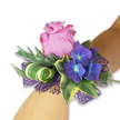 A modern romantic wrist corsage rests diagonally on a fair-skinned forearm, captured in soft, natural light that makes every texture visible. At its centre a velvety lavender-tinged rose unfurls in a generous, partially open bloom - petals layered with a faint blush and a touch of satin sheen that suggests a gentle, dewy perfume. Nestled close by are compact clusters of indigo-blue hydrangea; each tiny floret has a luminous, paler blue-to-white eye that seems to catch the light like a small twilight sky. The composition is framed by glossy variegated ivy leaves - deep green hearts edged with creamy yellow - which lend a classic, almost heirloom quality. Silvery-green sprigs, reminiscent of eucalyptus or dried lavender, provide a soft, wispy backdrop and a subtle savoury scent that contrasts the rose's sweetness. A contemporary flourish appears in a tightly curled, broad striped leaf with bold white and green banding, skillfully spiralled to add sculptural movement. Underpinning the flowers is a layer of open-weave deep purple mesh that peeks through, amplifying the hydrangeas' cool tones and giving the piece a refined, evening-ready lilt. The overall palette reads as cool and celebratory - mauve, deep indigo, and silvery green - and the textures invite touch: silky rose petals, papery hydrangea clusters, crisp ivy, and airy mesh. Designed with the precision of an experienced florist, this wristlet feels equally suited to a bridesmaid on a summer evening or a guest stepping out for a prom; it evokes calm joy and quiet confidence, like a small jewel that will be remembered long after the music ends.