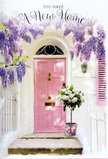 The image shows a gentle, romantic doorway that could easily sit on a quiet residential street near Temple Fortune, captured in soft daylight as if on moving day. A pastel pink front door, smooth and welcoming, is framed by whitewashed walls and a delicately painted shutter, setting a calm, uplifting stage. Above, wisteria trails in lush, cascading clusters of lavender and pale purple, each flower head composed of dozens of tiny blossoms that give the impression of a fragrant, tumbling curtain. Their shadows fall lightly across the façade, creating a dreamy interplay of light and shade. Resting on the stone doorstep is a grey, vintage-style metal bucket, brimming with white and creamy roses arranged with a florist's practiced eye. The roses are full and velvety, their petals gently unfurling, interwoven with soft green foliage that adds contrast and a sense of freshness, as though they were cut and placed only moments ago. A soft pink ribbon encircles the bucket, tied in a loose, romantic bow that spills over the side, echoing the door's hue and harmonising with the wisteria above. The composition feels quietly cinematic, like the still frame of a new chapter beginning - perfect for a new home card or a floral delivery to celebrate settling into Golders Green. As you imagine stepping closer, there is a sense of warmth, optimism, and shelter, as though every petal, vine, and ribbon is offering a wordless blessing of welcome, good fortune, and the comforting promise of many happy memories to come.