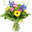 A richly coloured bouquet of fresh flowers stands upright against a pure white background, the crisp setting making every blossom and leaf appear vivid and clear. At the centre, fully opened pink roses reveal their layered petals, each bloom forming a soft, romantic cup of colour that draws the eye inward. Nestled around them, bright yellow gerbera daisies with striking dark brown centres introduce a playful, sunny contrast, their bold daisy faces giving the design a confident and uplifting character. Reaching higher than the other flowers, stems of deep blue delphinium create elegant vertical lines, the many small florets along each stem adding rhythm and a cool, tranquil counterpoint to the warmth of the pink and yellow. The bouquet is wrapped in a generous halo of greenery: delicate fern fronds spill gently from the sides, adding lightness and movement, while broad, glossy green leaves-some subtly striped-curve around the lower part of the blooms to form a neat, modern collar. Between the main flowers, clumps of bright green, textured filler foliage fill in the spaces like tiny cushions, enhancing the sense of fullness and structure. Fine, pale green stems tipped with tiny buds stretch upwards, contributing a lively, just-picked freshness reminiscent of early morning flowers sourced near Golders Hill Park. The stems at the base are neatly gathered and tied with a simple, natural-looking binding, clearly showing this as a hand-tied arrangement ready for delivery. Crafted with care by local florists in Golders Green, the bouquet feels joyful yet elegant, perfect for birthdays, congratulations, or bringing a burst of colour to a quiet corner at home.