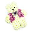A tender teddy bear-shaped floral tribute is presented here in clear, even light against a plain white background, allowing every thoughtful detail to be seen. The bear's entire body is composed of creamy white chrysanthemums, packed tightly together to form a plump, cuddly silhouette with a rounded head, soft ears, and short, reassuringly solid limbs. The petals layer over one another like tiny feathers, creating a texture that evokes the comforting feel of a much-loved soft toy. In the centre of the face, two small, dark eye details and a neat black nose are placed with precision, giving the bear an expression that is both gentle and quietly watchful. Just below, a slight curve of pale pink embellishment suggests a soft smile, as if the bear is offering calm support. Across the chest, a vest-like panel of deeper pink and mauve flowers adds an uplifting splash of colour, divided into two neat sections that frame the middle of the design. At the neckline sits a petite bow made of sheer purple netting, its delicate, gauzy loops providing a pretty contrast to the dense, rounded blooms beneath. The clean composition, with no surrounding objects or distractions, keeps the focus on the artistry and emotion within the tribute. In and around Golders Green, arrangements like this are often delivered to local chapels, funeral directors, or family homes as a gentle memorial for a child or a symbol of love at especially tender services. It communicates warmth, innocence, and ongoing affection, like a floral keepsake made to cradle precious memories.